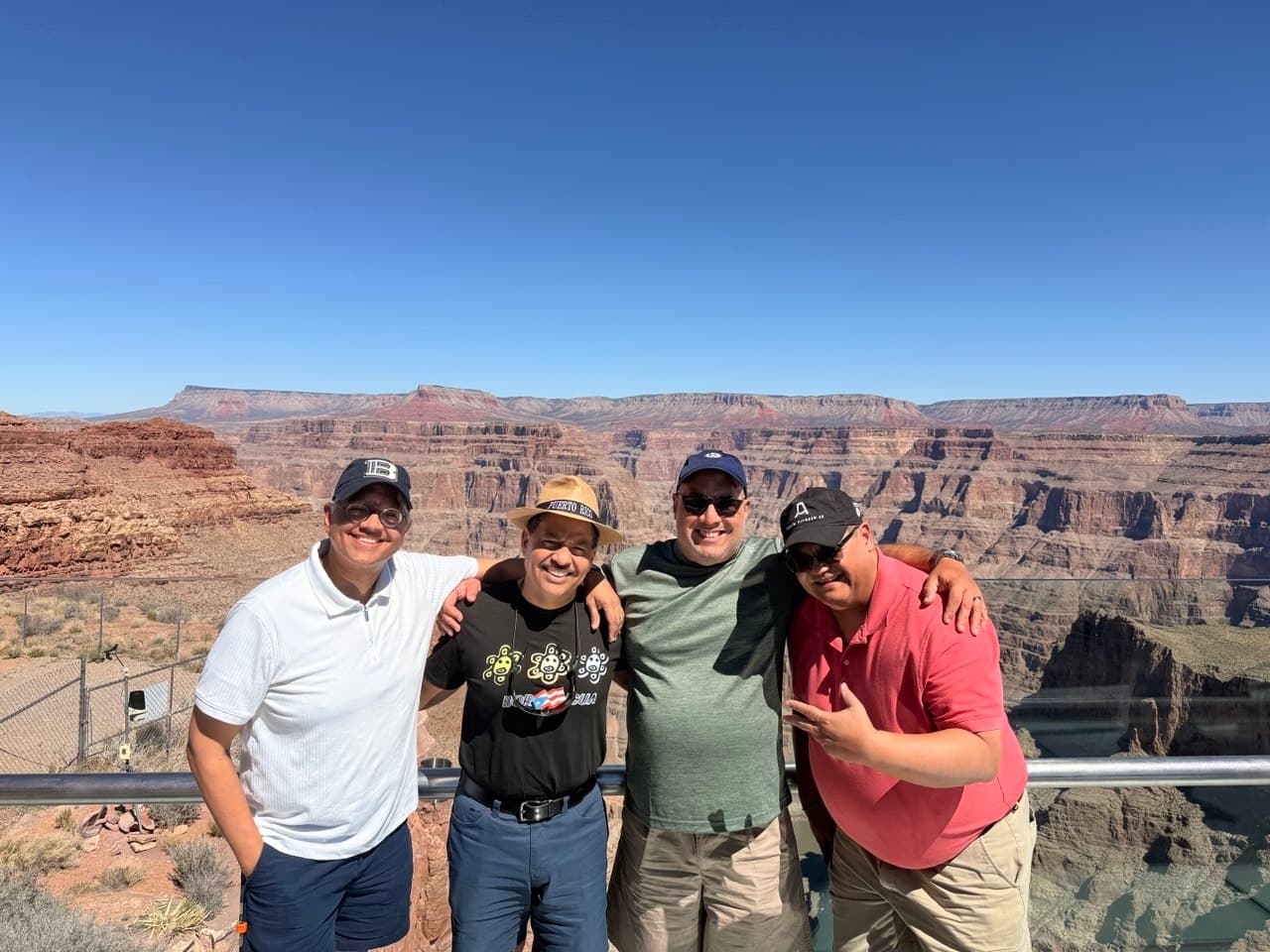The four friends arm in arm at the Grand Canyon Skywalk with the canyon behind them