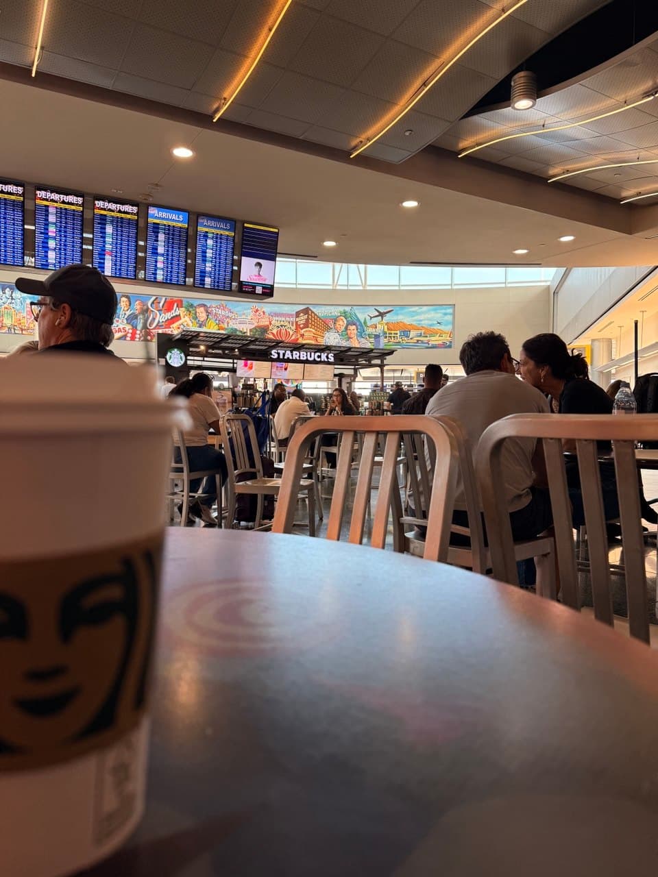 POV at the Las Vegas airport with a Starbucks cup and blue departure screens
